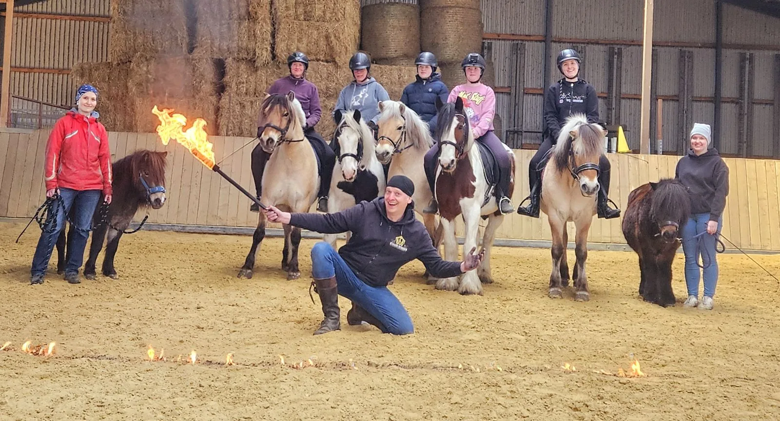 Kursgruppe mit Ponys und Trainer mit Feuerfackel im Reitstall